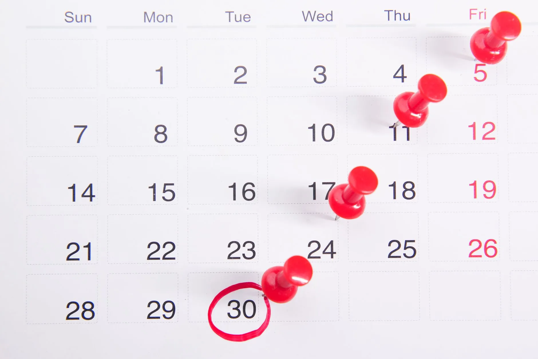 Calendario mensual con chinchetas rojas y una fecha rodeada que marcan vencimientos.
