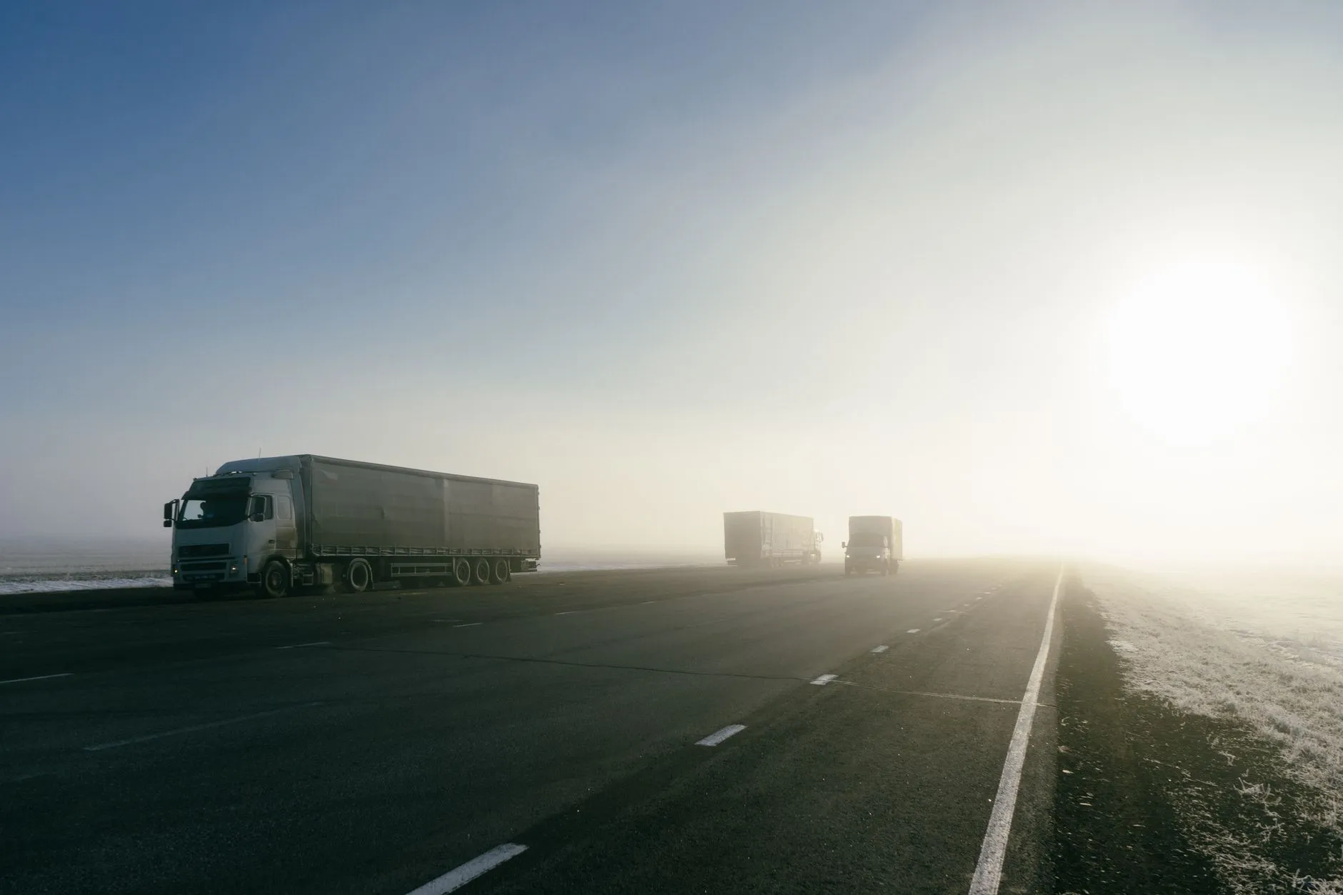 Camiones de transporte de mercancías circulando por una carretera al amanecer, con niebla