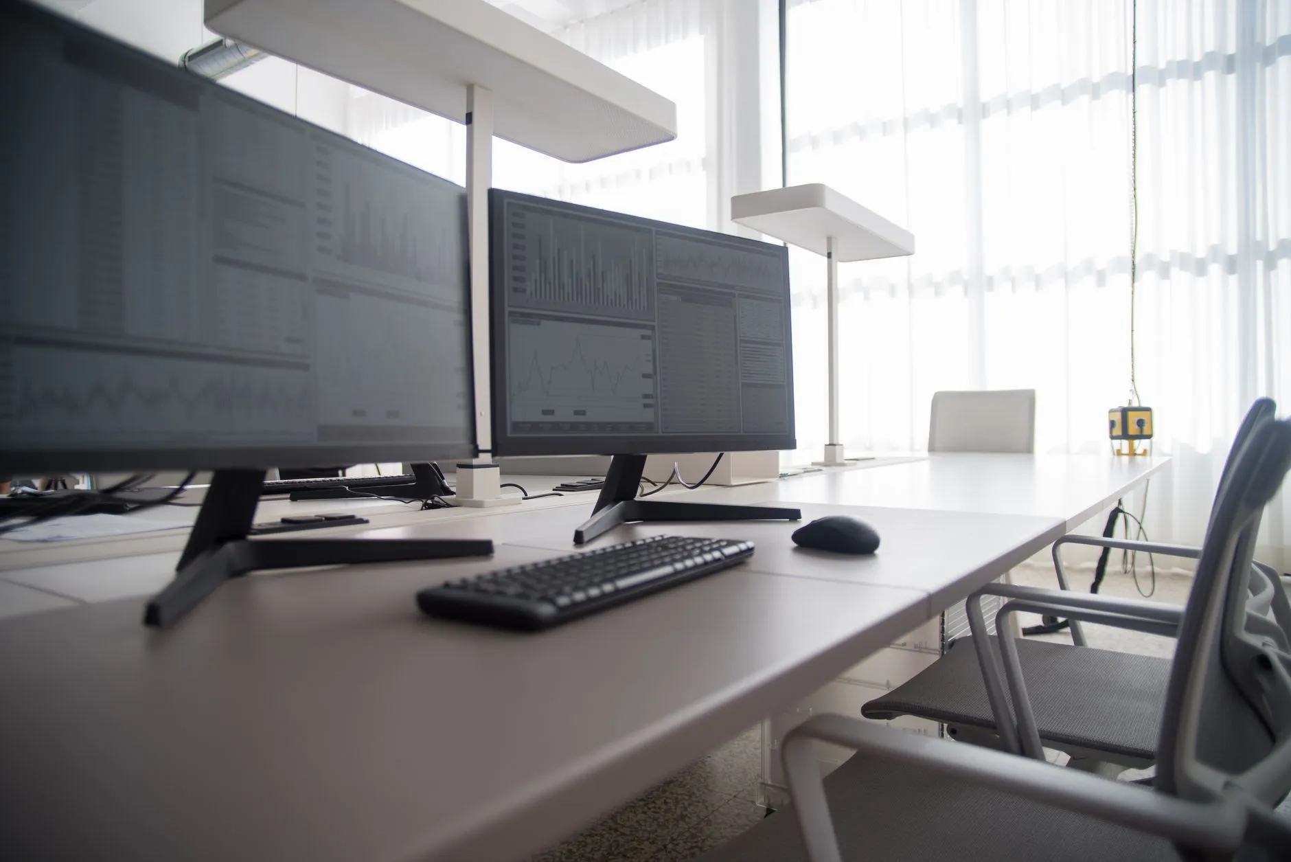 Puesto de oficina con dos monitores que muestran gráficos e informes, teclado y ratón sobre la mesa